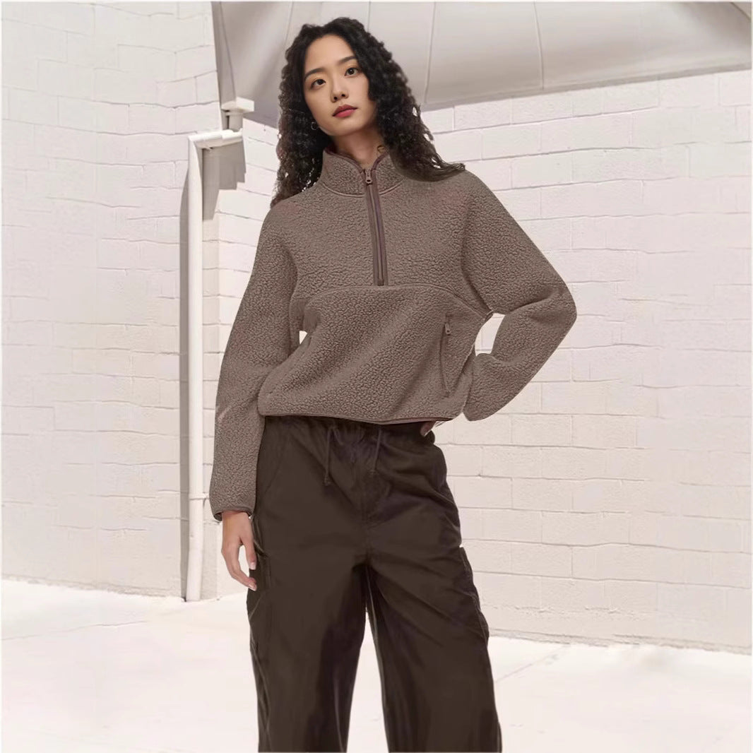 Woman wearing a brown lamb wool half-zip sweatshirt and black pants against white brick wall