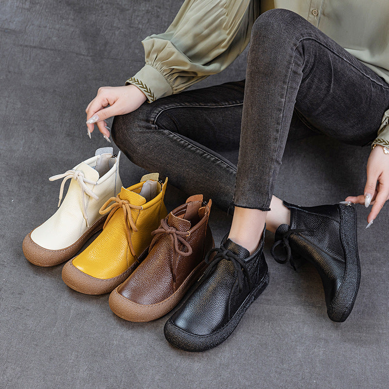 Woman wearing black leather lace-up ankle boots sitting next to white, yellow, and brown boots on gray floor