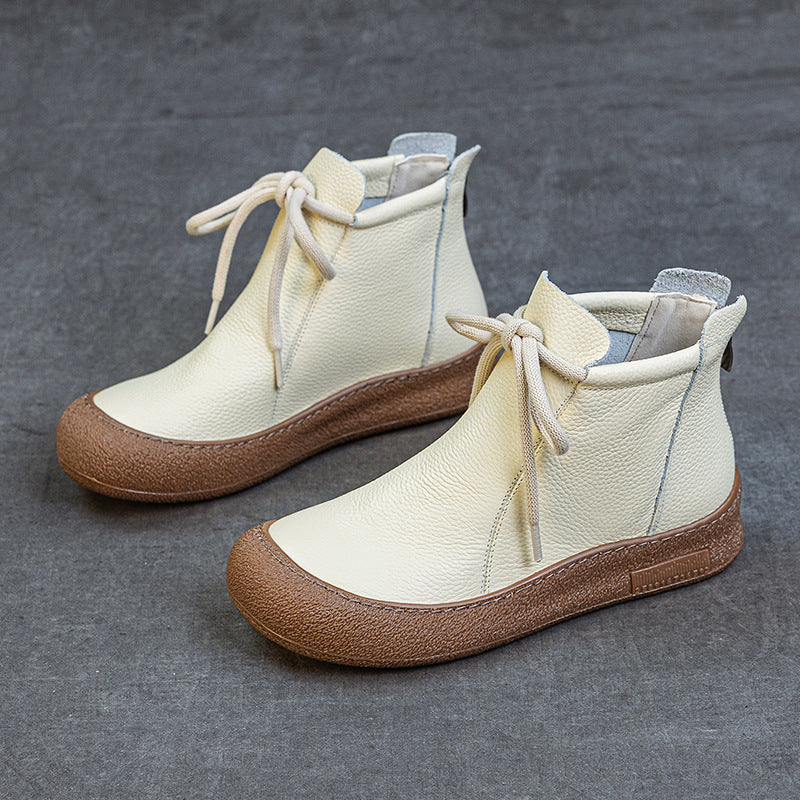 Cream leather ankle boots with brown textured rubber soles and beige laces on gray background