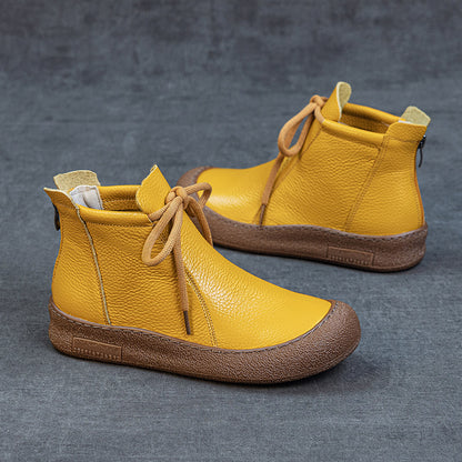 Yellow leather ankle boots with brown rubber soles and laces on gray surface