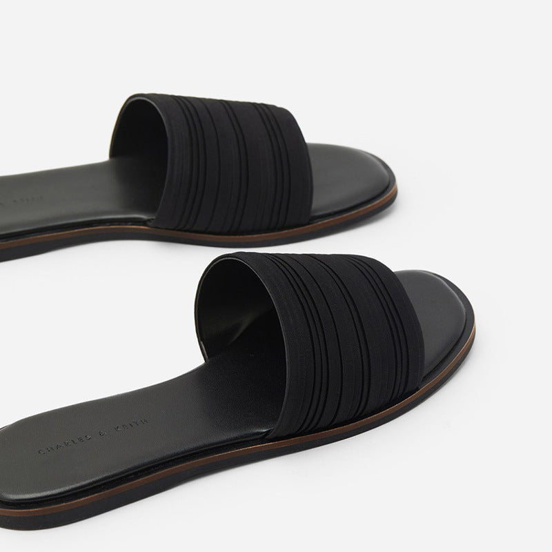 Black women's flat slide sandals with textured straps and brown trim on white background