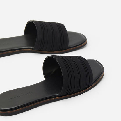 Black women's flat slide sandals with textured straps and brown trim on white background