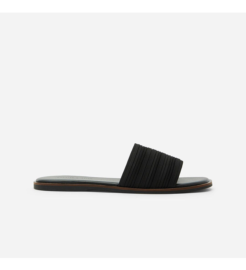 Black women's flat beach sandal with a wide pleated strap and thin sole on white background