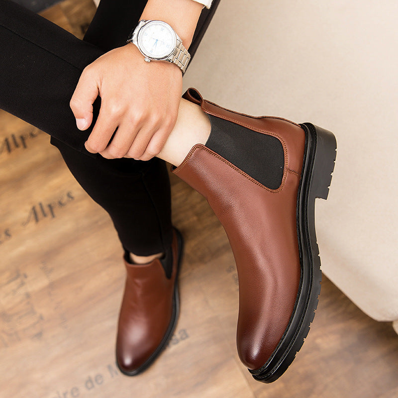 Close-up of brown leather Chelsea boots worn with black pants and a silver wristwatch on wooden floor
