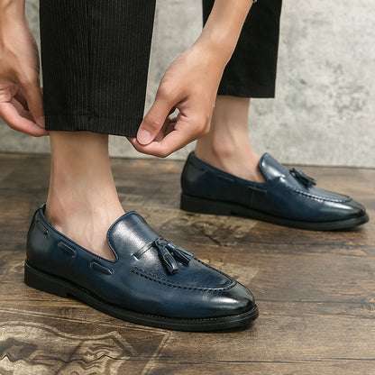 Men's navy blue leather tassel slip-on loafers worn with black trousers on wooden floor