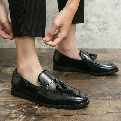 Men's black leather tassel slip-on loafers worn with black pants on wooden floor