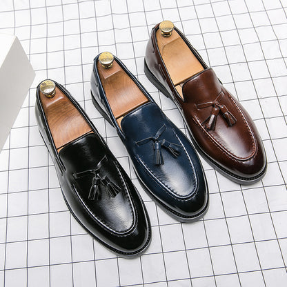 Black, navy blue, and brown men's tassel slip-on loafers in polished leather on white grid background