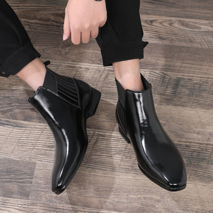 Men's black leather pointed-toe Chelsea boots with elastic side panels on wooden floor