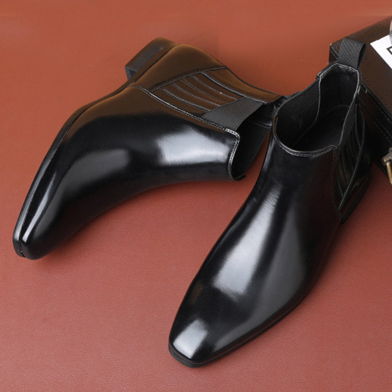 Black leather men's Chelsea boots with pointed toes and elastic side panels on brown surface