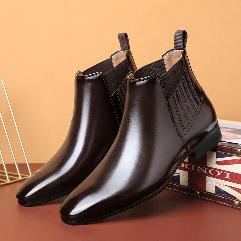Men's black leather Chelsea boots with pointed toe and elastic side panels on a brown surface