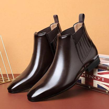 Men's black leather Chelsea boots with pointed toe and elastic side panels on a brown surface
