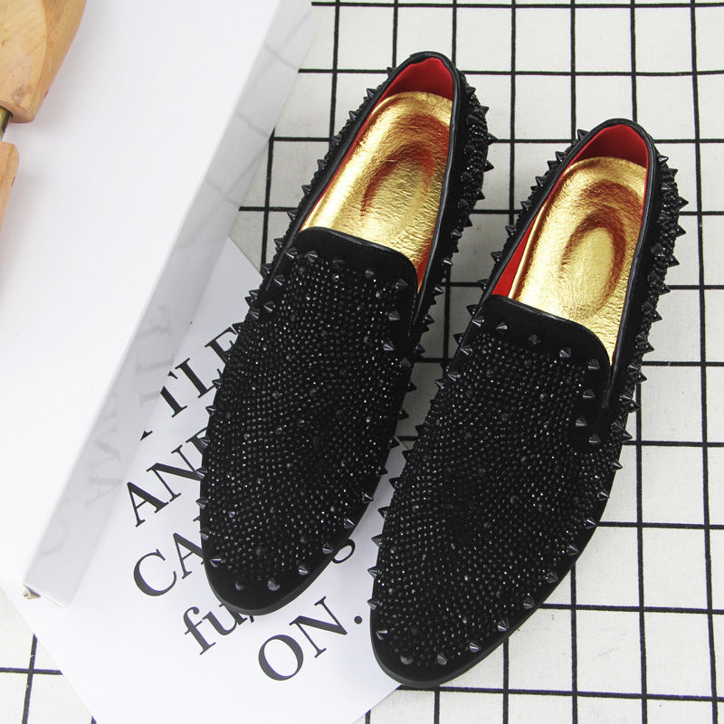 Black men's loafers with pointed toes, studded spikes, and gold inner soles on grid background