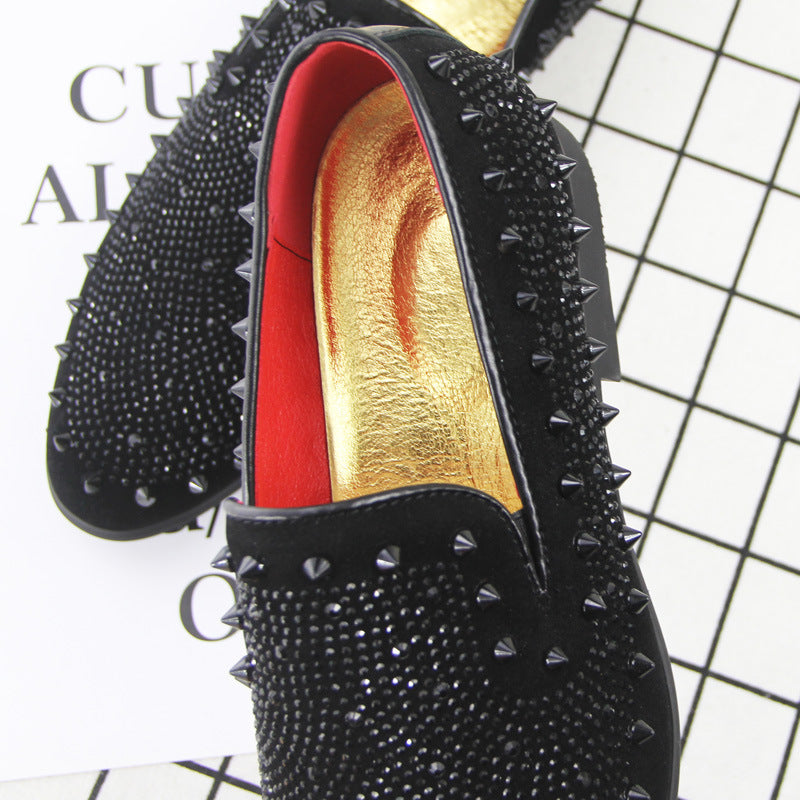 Black men's loafers with pointed toe, black spikes, red lining, and gold insole on patterned background