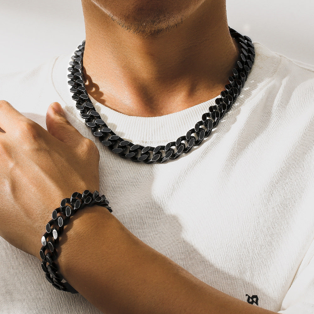 Man wearing black titanium steel Cuban link necklace and matching bracelet on white shirt