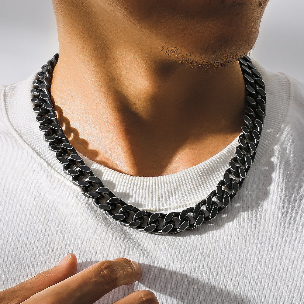 Close-up of a man wearing a durable 46cm black titanium steel Cuban link chain necklace with geometric design on white shirt