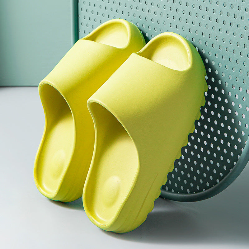 Yellow cushioned slide sandals with thick EVA sole against a perforated green backdrop