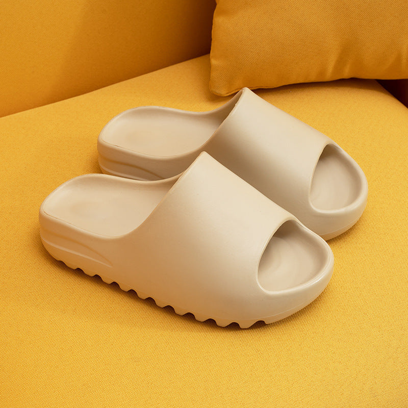 Beige cushioned EVA slippers with open toes resting on yellow fabric surface with a matching pillow