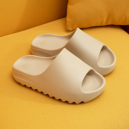 Beige cushioned EVA slippers with open toes resting on yellow fabric surface with a matching pillow