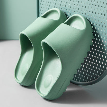 Pair of light green cushioned foam slides with thick soles resting against a perforated metal surface