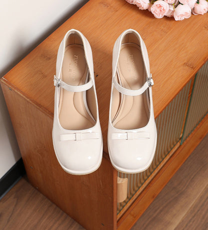 White patent leather Mary Jane shoes with bows on wooden cabinet and pink roses