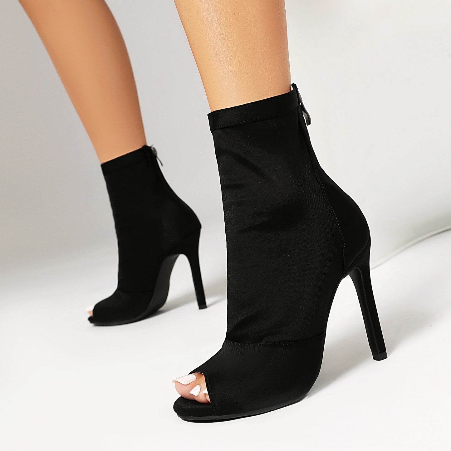 Black women's stiletto ankle boots with peep toe and back zipper on white background