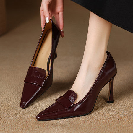 Woman wearing and holding dark burgundy leather pointed-toe stiletto pumps on carpet