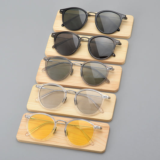 Five pairs of classic round sunglasses with titanium frames and polarized lenses in black, gray, clear, and yellow on wood blocks