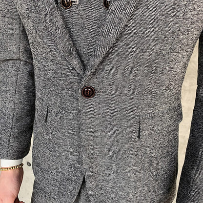 Close-up of a man wearing a gray herringbone patterned suit jacket with brown buttons and a gold bracelet