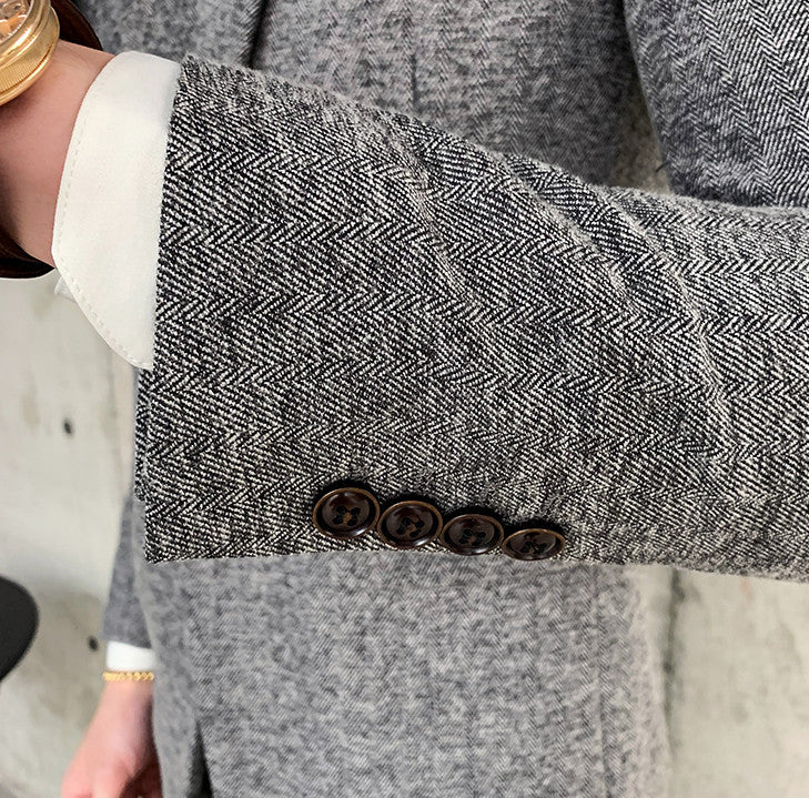 Close-up of a man's grey herringbone blazer sleeve with four dark buttons and a white shirt cuff