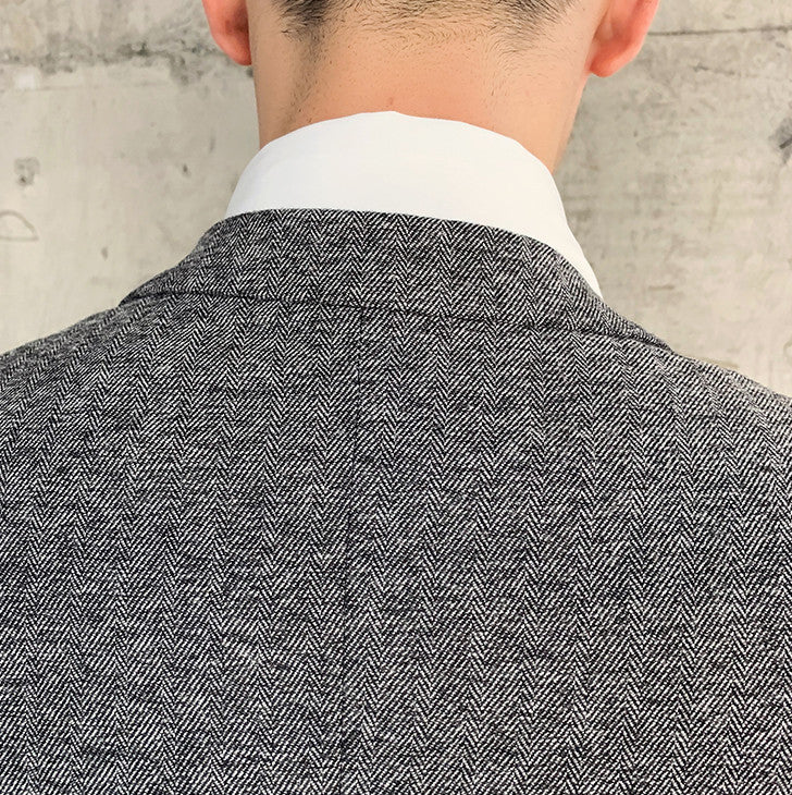 Back view of man wearing black men’s slim fit herringbone suit jacket with white shirt collar