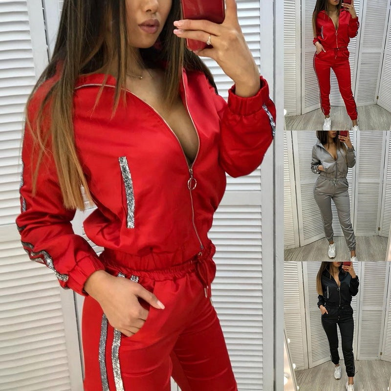 Woman wearing red two-piece sport suit with silver stitching, zippered jacket, and tapered pants in casual indoor setting