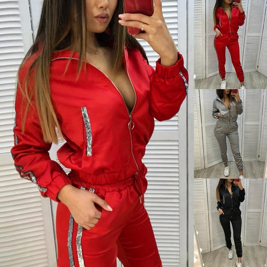Woman wearing red two-piece sport suit with silver stitching, zippered jacket, and tapered pants in casual indoor setting