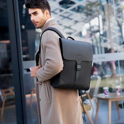Man wearing beige coat carrying black leather backpack with front buckle in urban setting