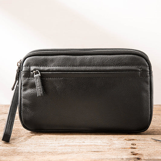 Black men's leather clutch bag with front zipper pocket and wrist strap on wooden surface