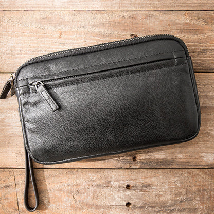 Black minimalist men's leather clutch bag with zipper on rustic wooden surface