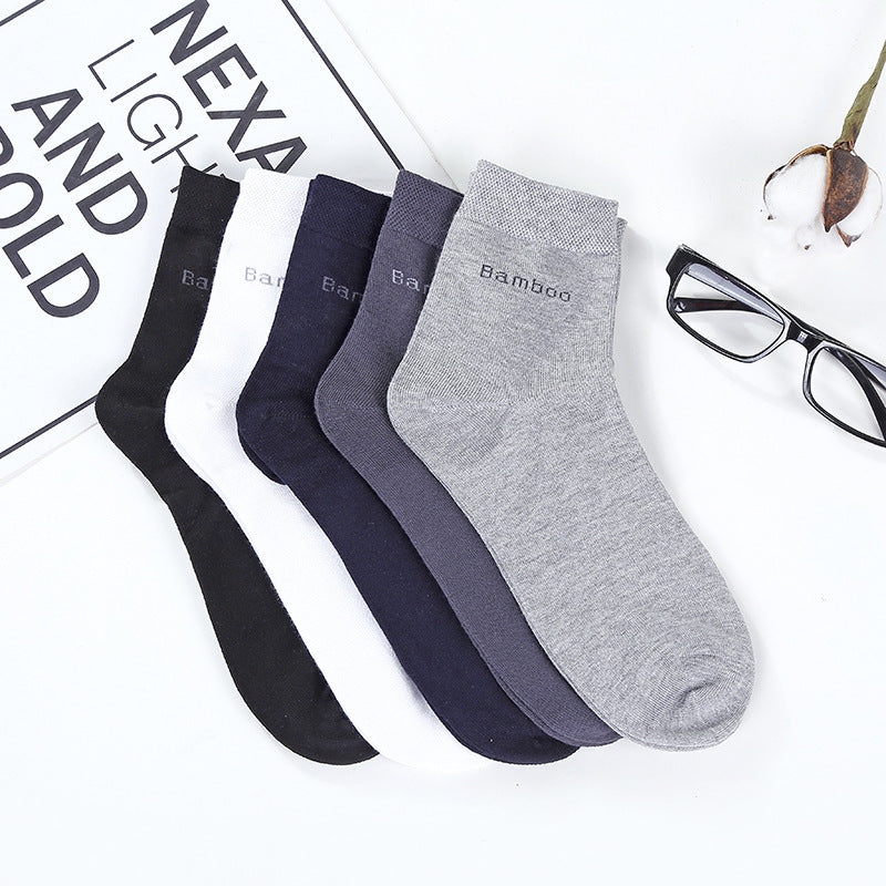 Set of five mid-calf bamboo socks in black, white, navy, dark gray, and light gray, displayed on a white surface with eyeglasses and a plant