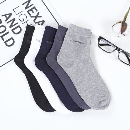 Set of five mid-calf bamboo socks in black, white, navy, dark gray, and light gray, displayed on a white surface with eyeglasses and a plant