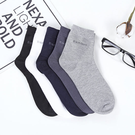 Set of five mid-calf bamboo socks in black, white, navy, dark gray, and light gray, displayed on a white surface with eyeglasses and a plant