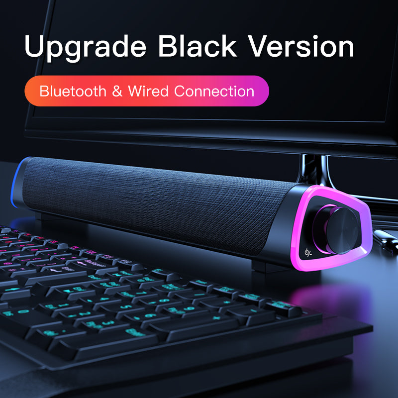 Black Bluetooth and wired soundbar with RGB lighting beside keyboard under monitor