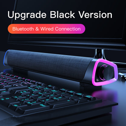 Black Bluetooth and wired soundbar with RGB lighting beside keyboard under monitor