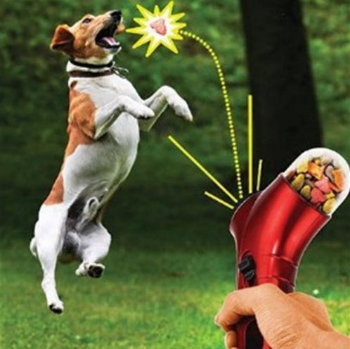 Interactive red pet treat launcher with ergonomic grip shooting treats for brown and white dog in grassy outdoor park