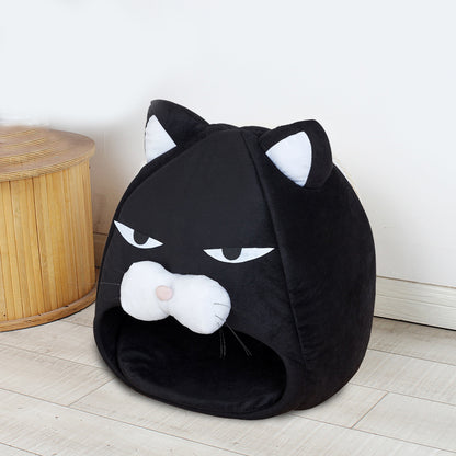 Black cozy cat bed shaped like a cat face with ears, white muzzle, and stitched eyes on wooden floor