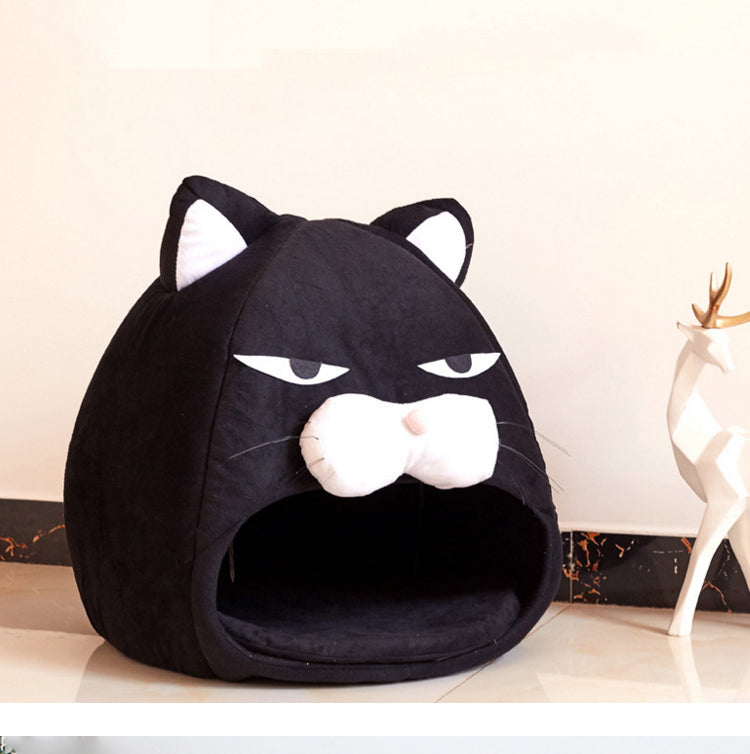 Black cozy cat bed shaped like a cat face with ears, white muzzle, and sleepy eyes on floor