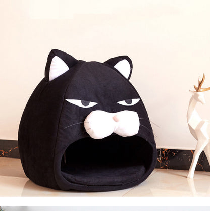 Black cozy cat bed shaped like a cat face with ears, white muzzle, and sleepy eyes on floor