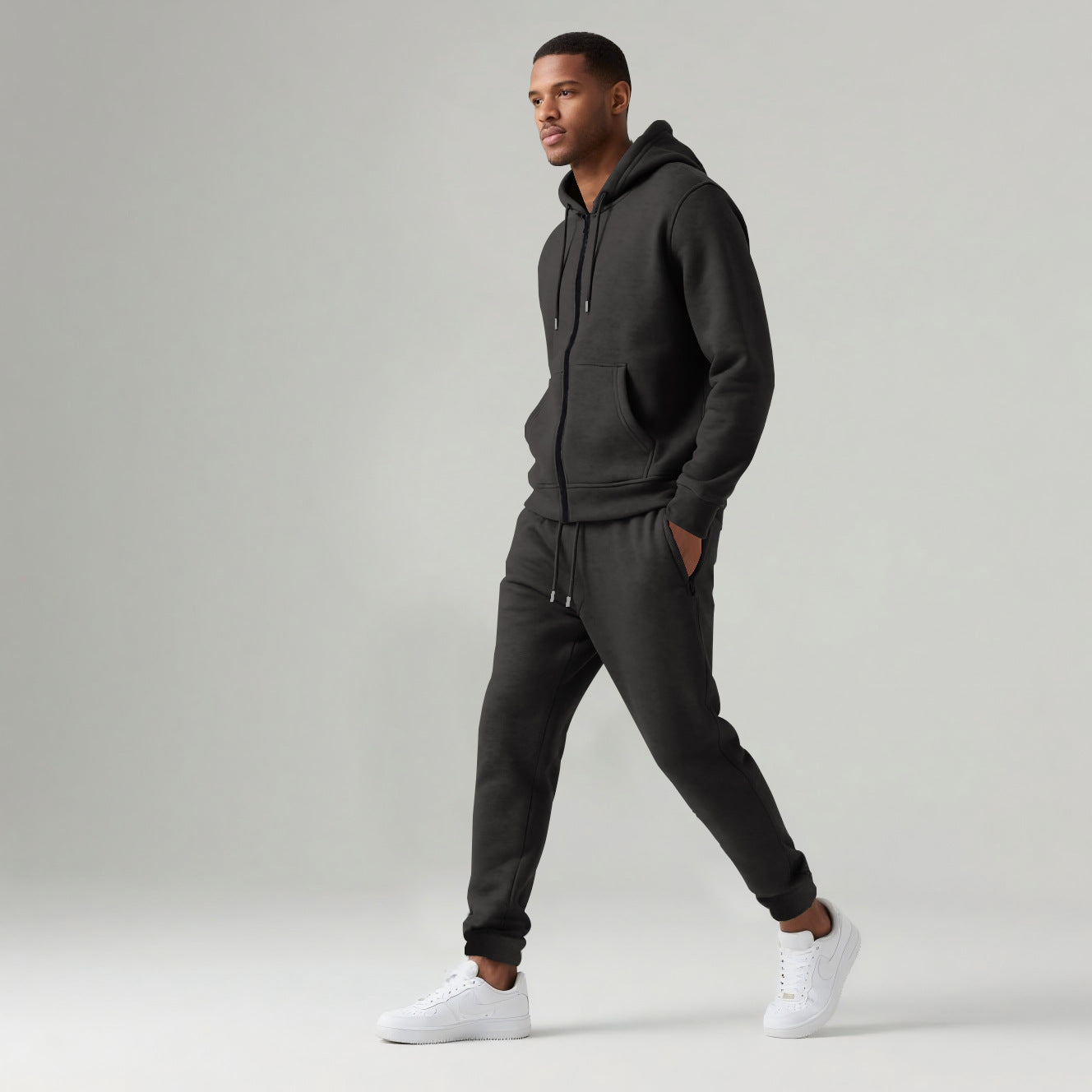 Man wearing black hooded zipped sportswear cotton blend tracksuit set with white sneakers on light background