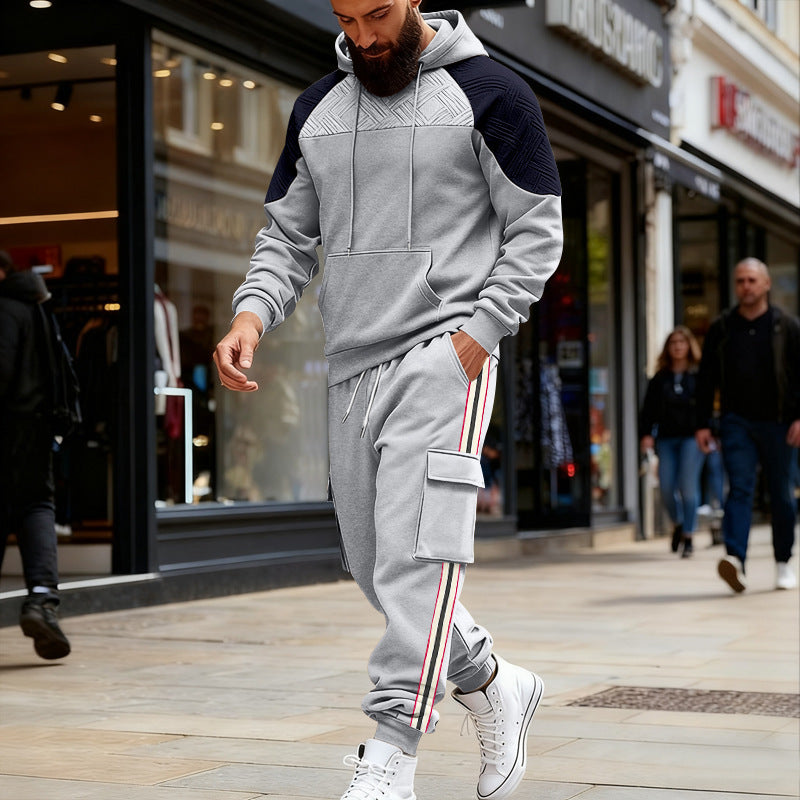 Bearded man wearing gray and black color block hoodie with matching cargo sweatpants and white sneakers walking in urban shopping area