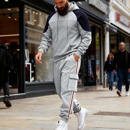 Bearded man wearing gray and black color block hoodie with matching cargo sweatpants and white sneakers walking in urban shopping area