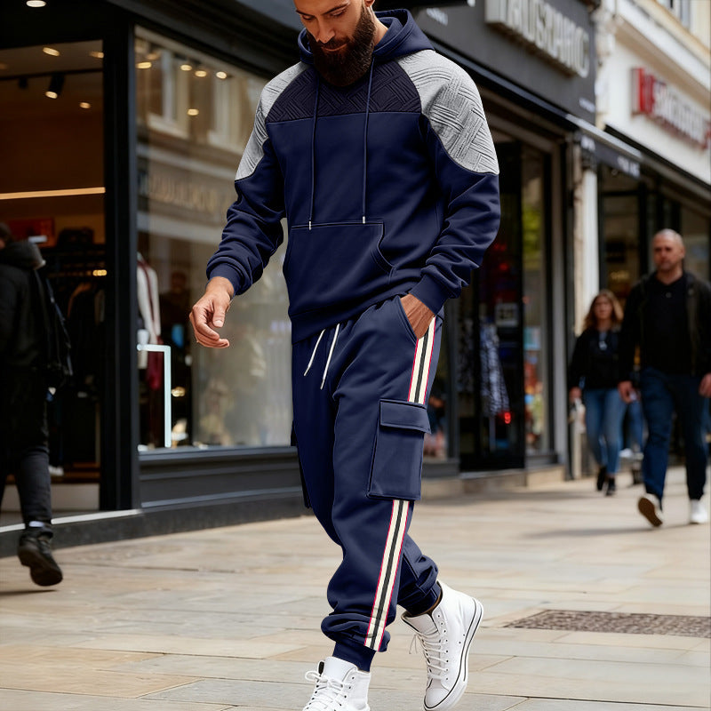 Man wearing navy blue and grey hooded sweatshirt and striped cargo sweatpants walking on city street