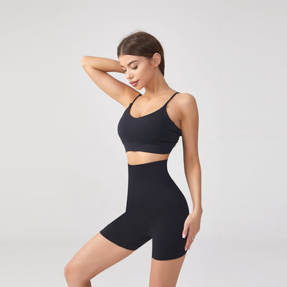 Woman wearing black seamless high-waist shaping shorts and sports bra on gray background