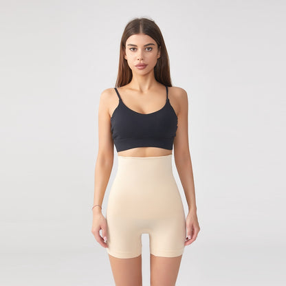 Woman wearing beige high-waist shaping shorts and black sports bra on gray background